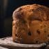 A round loaf of bread with a golden-brown crust and visible raisins on a wooden surface. - Olive Oil Times
