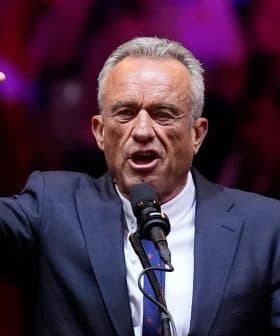 A man in a suit speaking passionately into a microphone while raising his hand. - Olive Oil Times