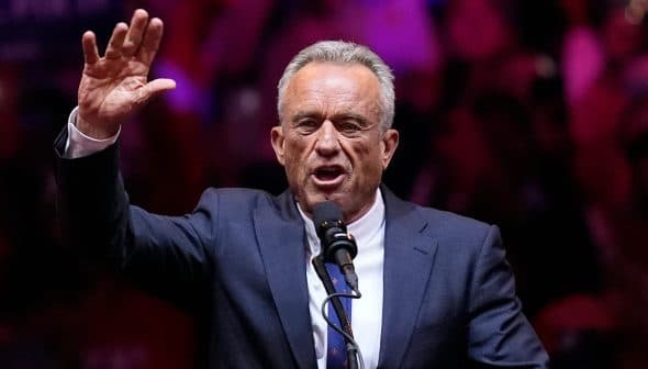 A man in a suit speaking passionately into a microphone while raising his hand. - Olive Oil Times