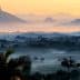 A misty landscape featuring mountains and valleys during sunrise with soft light and fog. - Olive Oil Times