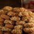 A large stack of honey-dipped cookies topped with crushed nuts on a wooden surface. - Olive Oil Times