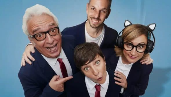 Four individuals posing together, two wearing glasses and one with headphones, all in formal attire with blue background. - Olive Oil Times