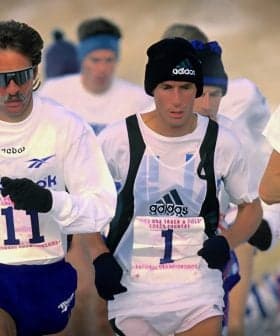Three male runners participating in a competitive race, wearing athletic gear and numbers on their shirts. - Olive Oil Times