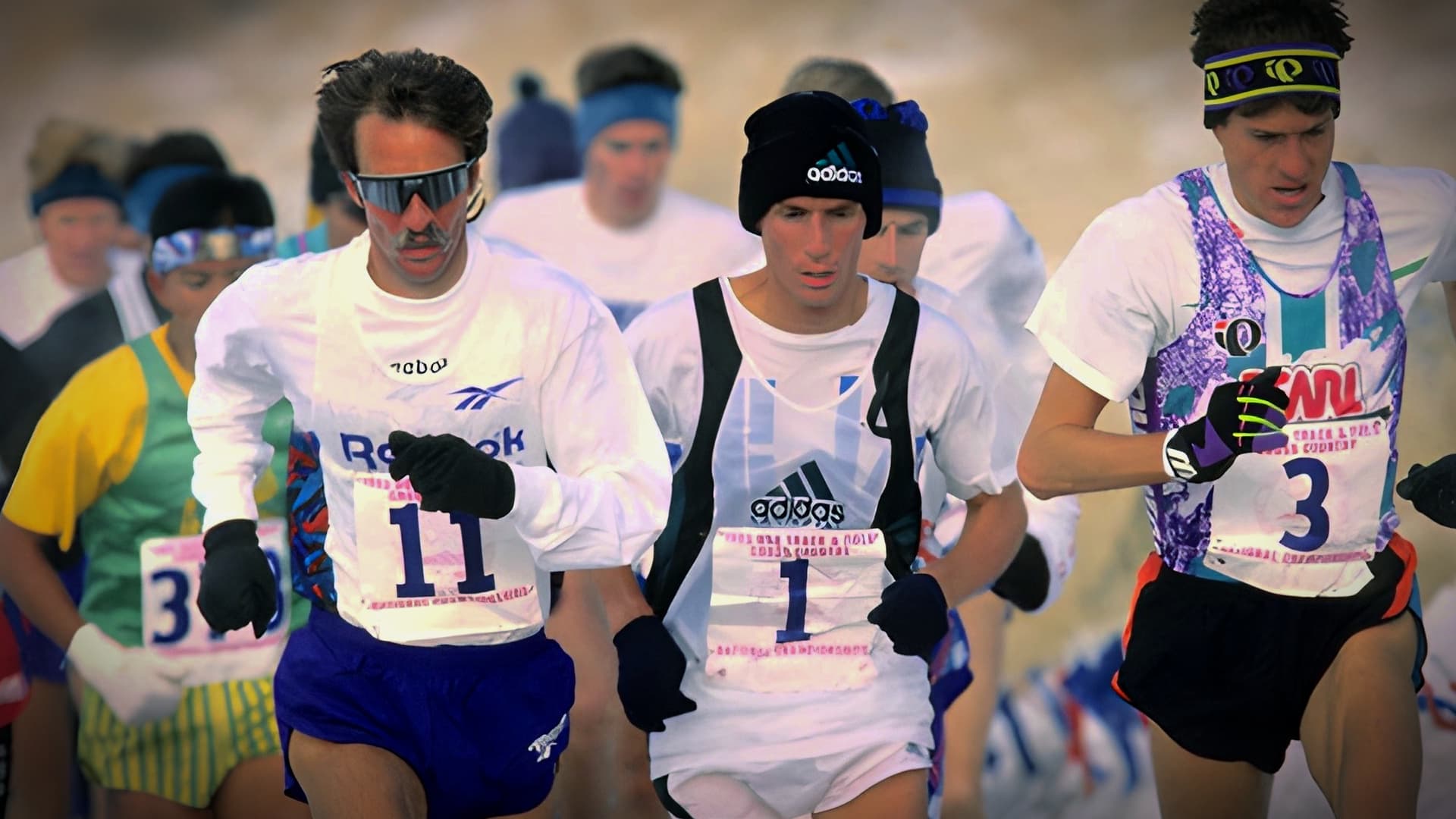 Three male runners participating in a competitive race, wearing athletic gear and numbers on their shirts. - Olive Oil Times