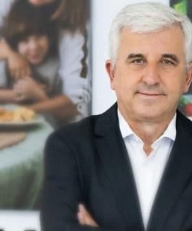 A man with white hair wearing a black suit, standing with arms crossed in front of a blurred background. - Olive Oil Times