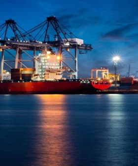 Large container ship docked at a port with cranes and cargo containers under a night sky. - Olive Oil Times