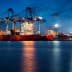 Large container ship docked at a port with cranes and cargo containers under a night sky. - Olive Oil Times