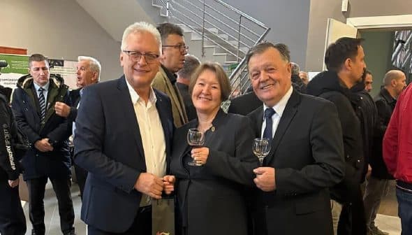 Three individuals standing together, each holding a glass, in a gathering or event setting. - Olive Oil Times