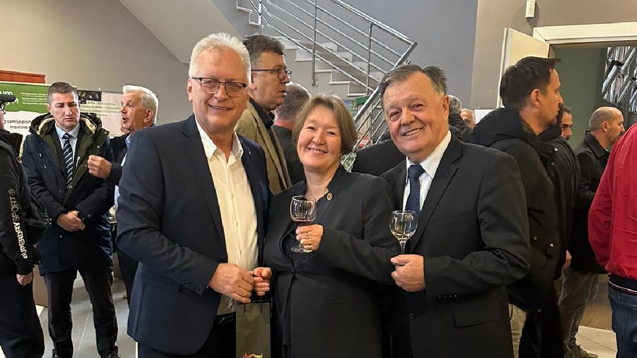 Three individuals standing together, each holding a glass, in a gathering or event setting. - Olive Oil Times