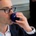 Man wearing glasses drinking from a blue glass with the word 'Olive' on it. - Olive Oil Times