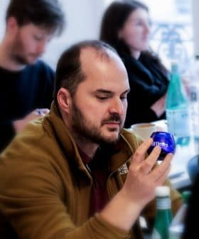 Man examining a blue olive oil bottle while seated in a seminar with other attendees in the background. - Olive Oil Times