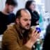 Man examining a blue olive oil bottle while seated in a seminar with other attendees in the background. - Olive Oil Times