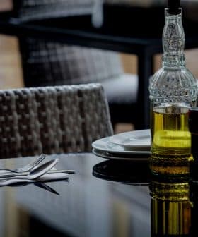 Glass olive oil bottle with a decorative design next to salt and pepper shakers on a table. - Olive Oil Times