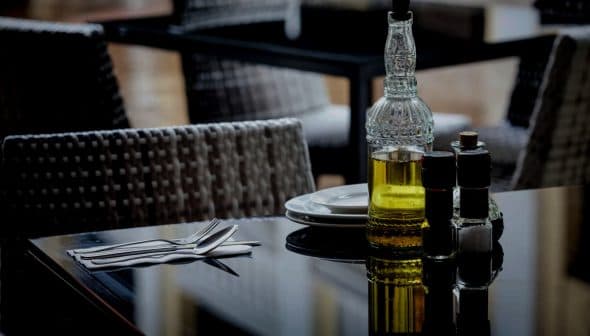 Glass olive oil bottle with a decorative design next to salt and pepper shakers on a table. - Olive Oil Times