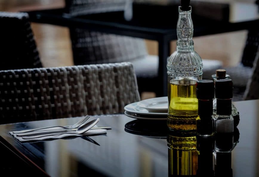Glass olive oil bottle with a decorative design next to salt and pepper shakers on a table. - Olive Oil Times