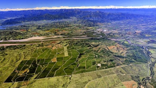 Aerial view showing extensive agricultural fields and mountainous terrain under a clear sky. - Olive Oil Times