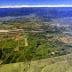 Aerial view showing extensive agricultural fields and mountainous terrain under a clear sky. - Olive Oil Times