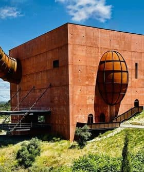 A large, red architectural building with a prominent spherical and cylindrical design element. - Olive Oil Times