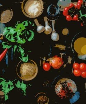 An overhead view of various cooking ingredients including vegetables, herbs, and spices on a wooden surface. - Olive Oil Times
