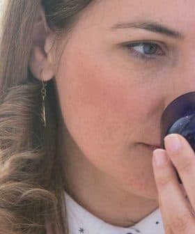 Woman with curly hair holding a blue glass container to her nose while smelling its contents. - Olive Oil Times